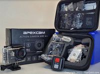Photo showing Apexcam Action Camera M80 Air in waterproof housing, remote control, multiple mounts/accessories in plastic bags, and protective black storage case.
