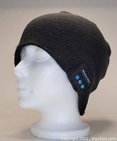 Black knit toque hat on mannequin head showing Bluetooth control panel with buttons.