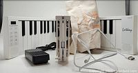 Foldable 88-key white piano keyboard with black keys unfolded and accessories including a black sustain pedal, a USB charging cord, and beige fabric carrying case.