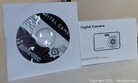 Photo shows a driver disk for camera software and an instruction manual for the digital camera with a camera diagram on the front, indicating the accessories that come with the digital camera.
