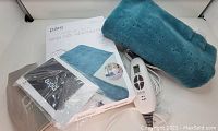Photo showing the blue rectangular heating pad folded with white wired LED controller, product manual, and storage bag.