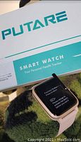 Putare smart watch with rectangular screen showing a prompt on a grassy background with box in the background.