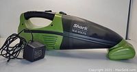 Photo of the Shark cordless handheld vacuum in black and green, with charger attached. Shows the full profile and condition of the vacuum.