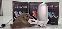 Three silver double-sided rechargeable electric hand warmers with boxes, charging cords, and soft carrying pouches shown on a white surface.