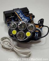 Black rechargeable headlamp with five LED lights and three adjustable straps labeled 'HEADLAMP'. USB charging cable included.