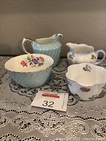 Two sets of creamers and open sugar bowls, one light blue and ribbed with floral interior, the other white with floral patterns.