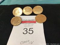 Five Canadian Olympic dollar coins arranged on a black cloth, showing front sides with detailed Olympic imagery, various athletes and the Olympic rings, and maple leaf symbols. Coins show wear consistent with circulation.