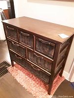 Full view of wooden 6 drawer cabinet with woven wicker basket drawers, standing on wooden legs, placed on a rug.