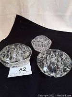 Three clear crystal flower frogs displayed on a black background showing top and side views with round shapes and multiple holes for floral arrangements.