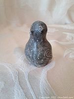 Front and side view of the small dark soapstone owl figurine with incised detailing on wings and body.
