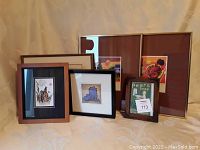 Full view of six framed prints grouped together on beige surface showing variety of sizes and frame styles.