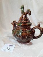 Front and side view of the vintage majolica rooster teapot showing detailed rooster lid and spout design with embossed decorations.