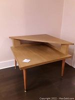 Full side view of mid-century modern style 2-tier wood corner table, showing triangular top tier and square bottom tier with tapered legs.