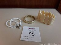 Set of 3 bracelets displayed on white surface with auction card: vintage white milk glass bead bracelet, natural organic material cuff, signed Lia Sophia stretch bangle.