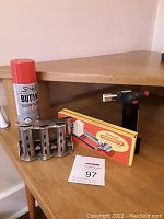 Photo showing brulee torch, butane fuel can, and metal coin dispenser on wooden shelf