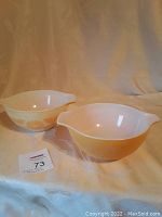 Two Pyrex mixing bowls side by side, showing yellow and white floral exterior design and integrated handles/spouts