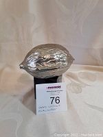 Front view of silver-tone walnut-shaped nutcracker with textured detail, sitting on black stand.