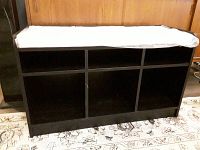 Front view of dark wooden shoe bench with five open cubbies and cushioned top still in plastic