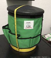 Front view of yellow bucket tool organizer with black lid and green fabric organizer showing multiple external tool pockets and tape measure to indicate height.