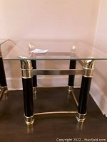 Photo of 1980s Italian style black and brass side table with clear glass beveled top, showing table fully with legs and brass details visible.