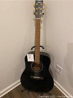 Front view of Yamaha black lacquer acoustic guitar on stand showing headstock and body
