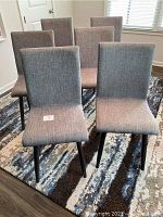 Six grey upholstered dining chairs arranged on a rug