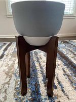 Front view of the grey and white ceramic planter sitting on the walnut-colored wooden stand on a patterned carpet.