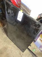 Black flat screen TV leaning against a wall showing reflective screen surface.
