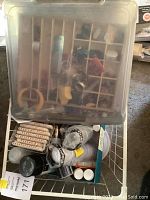 Storage case with small beads and craft embellishments including feathers and small tools.