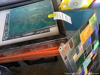 Stack of framed artworks including multicolored mosaic glass tile artwork and turquoise skull art.
