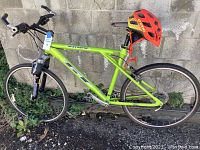 Side profile of green GT Avalanche bike leaning against block wall with orange helmet on seat post