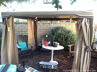 Full exterior view of tan canopy with black metal frame and tied-back curtains