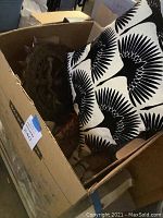 Box containing black and white cushion with bird pattern and the metal sculpture partially visible