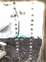 Overall view showing two vertical strings of colorful metal birds hanging outdoors next to a wooden chair and hammock.