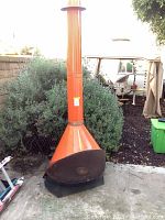 Full front view of orange metal chiminea against garden backdrop