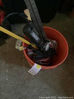 Photo of orange bucket containing Rockwell electric miter saw and various hand tools including measuring tape and carpenter's square.