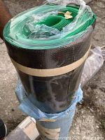 Photo of tightly rolled new 44 inch wide rug pad with black textured surface and green backing, secured with tape and plastic wrapping.