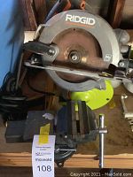 Close-up image of Ridgid circular saw with rusted blade and gray bench vise mounted on a wood surface.