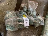 Seven clear plastic zip-lock bags filled with raw turquoise chunks on concrete floor.