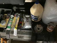 Top view of woodworking adhesives, sharpening tools, wire brush, steel wool, and flashlight arranged on black toolbox.