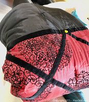 Close-up photo of a folded queen size comforter showing black and red fabric with black scroll patterns