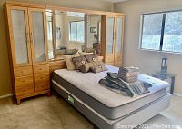 Overall view of the bed frame with mattress, pillows, and linens in a carpeted bedroom with a window and side table.