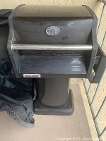 Front view of black Brinkmann charcoal grill with stainless steel handle, closed lid, standing on pedestal base, outdoors.