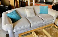 Front view of the white textured fabric couch with three seat cushions and three pillows (two aqua, one white) placed on it.