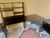 L-shaped black desk with attached shelving on wall corner, brown floor mat underneath