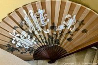 Large decorative fan with floral pattern in brown, white, and black hanging on wall.