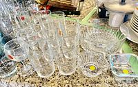 Overview of assorted clear and colored glassware on kitchen counter including Coca-Cola branded glasses, bowls, and holder.