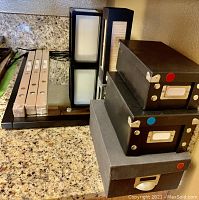 Photo of three Ikea TJUSIG window shades in packaging, black lamp with frosted glass panels, three black storage boxes stacked, and black metal incense burner