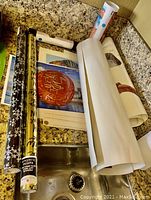 Photo showing rolled prints, posters, and rolls of Christmas wrapping paper on a kitchen countertop and sink.