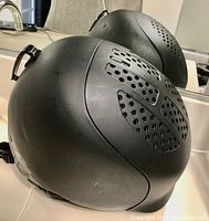 Black ski helmet with vent holes shown on a counter reflecting in a mirror